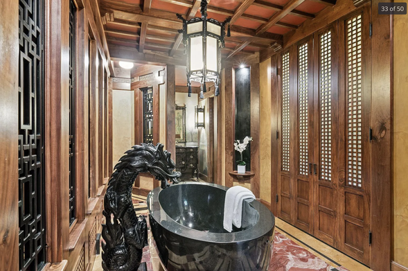 A very large bathroom with Japanese style woodwork and geometric patterns. There is a large solid marble bath in the middle with a carved dragon which is the water spout.