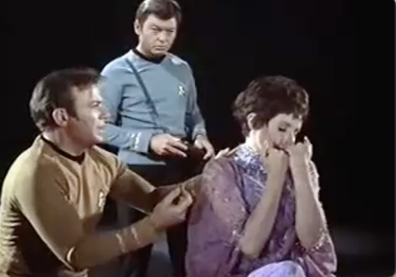 Still frame from Star Trek Original Series episode "The Empath". Kirk tries to talk to a silent empath while she holds up her hands to her face as, looking as if she is smelling her dress.