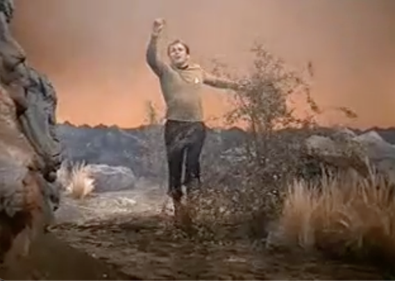 Captain Kirk runs - slowly - towards the camera of destroyed planet with a rust orange sky.