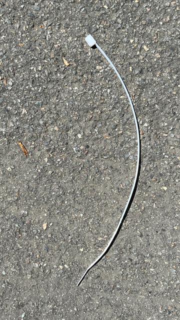 a plastic zip tie, shaped as the curve of a comma, sitting on asphalt in the sun