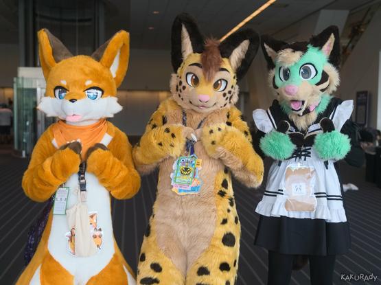 An orange shiba inu fursuiter, a yellow serval fursuiter, and a green and tan fursuiter in a French maid outfit standing side by side in a carpeted hallway. The left fursuiter has their hands on their chest. The two fursuiters on the right have their palms facing inward, two index fingers touching as if shy or embarrassed. In the background there are an escalator and a glass walled elevator shaft, in front of unmarked gates lit from the transom.