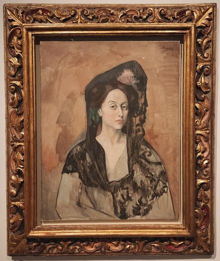 Bust portrait of a Spanish woman in beige-dark brown tones. She is wearing a loose-fitting beige dress and a black veil that covers her entire shoulders and is held aloft above her head by a hat or hairpin.