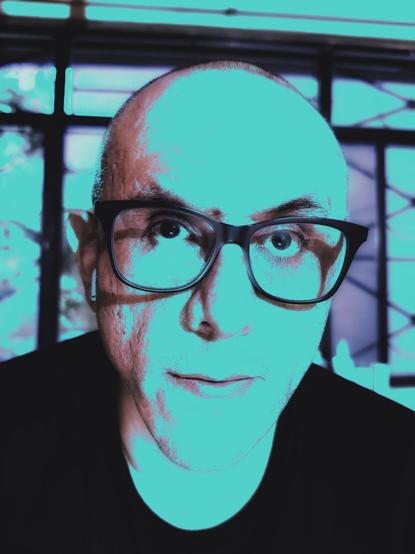 Una imagen de color falso de un hombre de mediana edad con la cara larga, lentes negros y la cabeza rasurada.