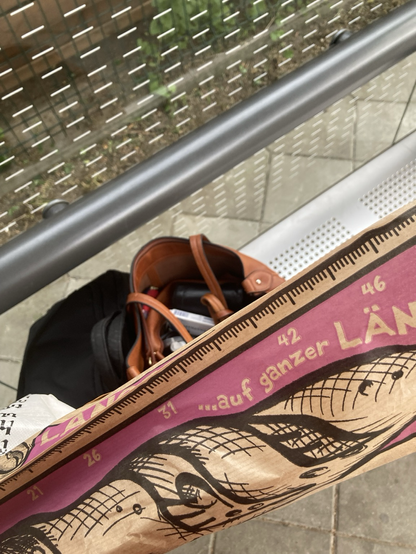 Schwarze Laptoptasche, brauner Ledershopper und Papiertüte von Bäckerei auf Bank in Wartehäuschen.
