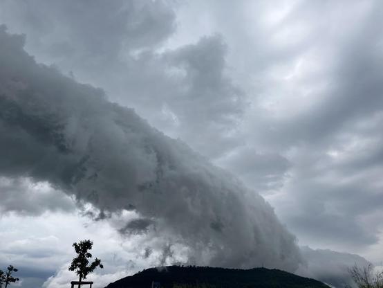 Ein graues Wolkenband, das über einen Berg zieht.