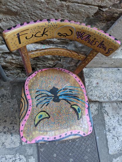 Old chair painted with a cat face and the words 'fuck whiskas'
