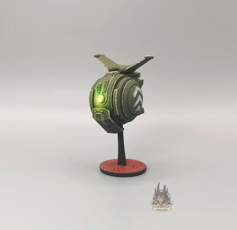 Drone - it's spherical with stablising fins at the top, in a drab green with grey chevron patterns on the side panels - front right view