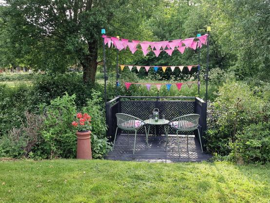 A bunting decorated deck in a garden overlooking a public green space