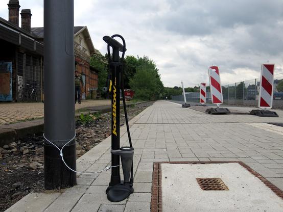 Eine Luftpumpe steht vor einer Straßenlaterne. Die Pumpe ist mit einem Drahtseil an der Laterne befestigt.