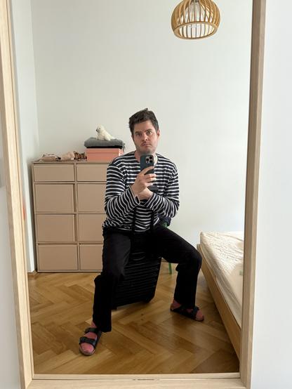 Spiegelselfie: Moritz sitzt missmutig auf einem ganz normalen kleinen schwarzen Rollkoffer