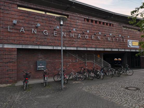 Wer hätte das gedacht: Langenhagen Mitte steht an der modernen Backsteinfassade, schmucklos und doch um Aufmerksamkeit bittend. Fahrräder sind davor angestellt, graues Steinpflaster und eine Laterne runden das Ganze ab.