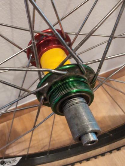 Foto einer dreifarbigen Fahrradnabe (rot-gelb-grün) mit Schraubgewinde und beschädigten Speichen.