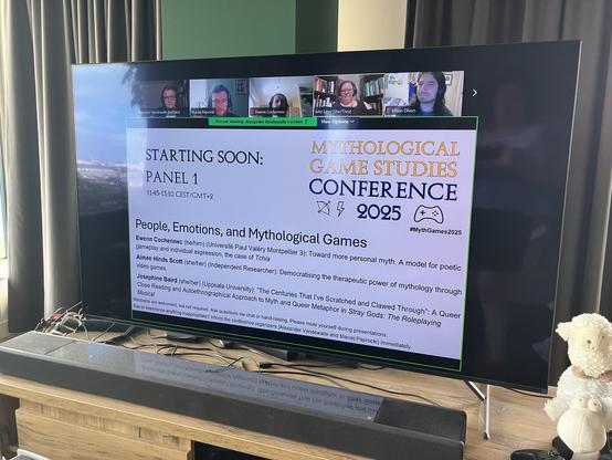 Pic of a TV showing a slide of the conference, with the lineup for the first panel.