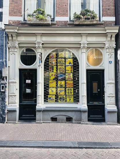 Window of Wax Well Records in Amsterdam. 3 by 7 grid of records. Mostly yellow, among them are albums by: De La Soul, Queen (Flash Gordon), Dizzy Rascal, the B52’s, Chuck Berry and the Kill Bill Soundtrack.