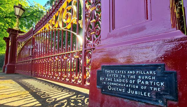 A sign in a set of large, ornamental cast-iron gates which reads These gates and pillars gifted to the burgh by the Ladiea of Partick in commemoration of the Queen's Jubilee.
