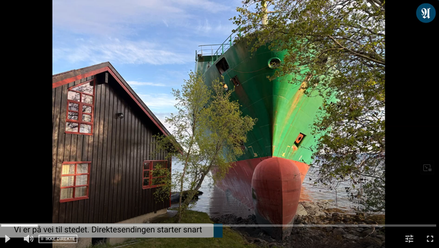 Screenshot eines Livestreams, links ist ein Holzhaus an einem Fluss, direkt daneben ist ein rot-grünes Schiff (das höher als das Haus ist) im Ufer festhängend.