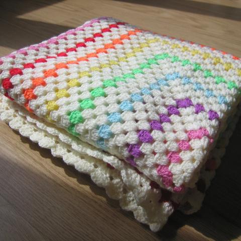 A picture of a folded up crochet blanket that's white and rainbow colored.