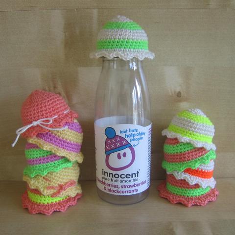 A picture of a plastic bottle of the brand 'innocent' with a tiny crochet hat on, with a variety of crocheted hats around it in neon colors.