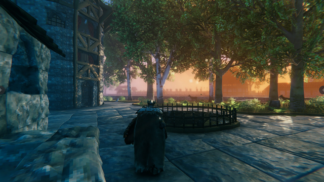 Valheim Screenshot: Links im Bild ein steinernes Gebäude, vielleicht der Eingang einer Burg. Rechts sind einige Bäume und dahinter lässt sich eine Stadtmauer erahnen.