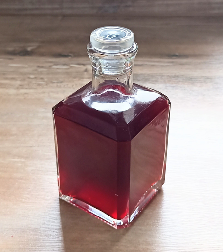In einer viereckigen Glasflasche  der tiefrote Himbeeressig