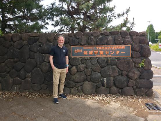 Me standing in front of a wall at the entrance of JAXA's Tsukuba Space Center