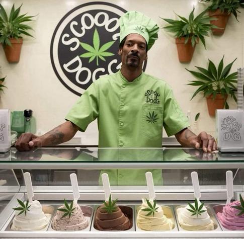 Snoop Dogg, rap and marijuana icon dressed as ice cream seller behind seven flavors and in front of a sign that reads SCOOP DOGG...