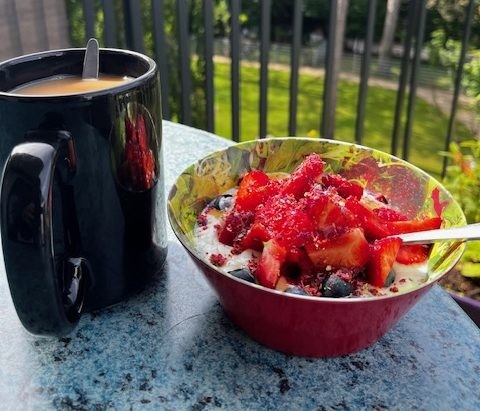 Schüssel mit Müsli und Erdbeeren sowie eine schwarze Tasse mit Tee und Milch