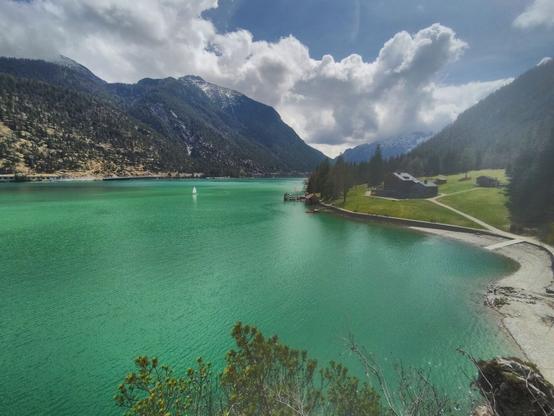 Fair weather at the Achensee: The photo is taken at a viewpoint near the Gaisalm. The lake's water appears very green while the sky is blue. Some grey clouds can bee seen above the mountains at the opposite lakeside.
