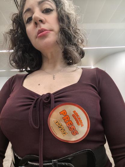 Laura con una blusa morada escotada. Sobre el pecho, una pegatina que la acredita como Arcadia Group Press
