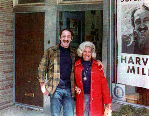 Milk (with mustache and plaid shirt), here with his sister-in-law in front of Castro Camera in 1973, had been changed by his experience with the counterculture of the 1960s. Dianne Feinstein, who first met him in 1973, did not recognize him when she met him again in 1978. By Unknown family member - Provided by Stuart Milk, CC BY-SA 3.0, https://commons.wikimedia.org/w/index.php?curid=5113141