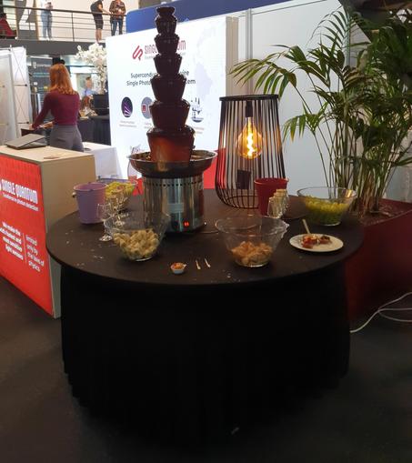 Photo of a big chocolate functions with an assortment of fruits, next to it a booth of a company called Single Quantum