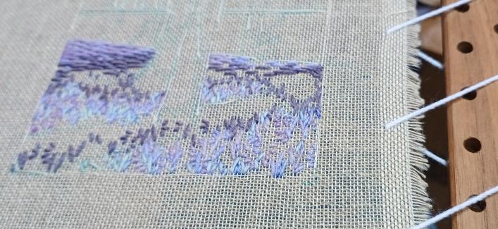 A part worked, stitched artwork in shades of purple, lilac and blue