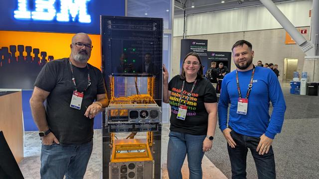Trio of IBMers at the IBM booth standing next to the IBM LinuxONE 5 plexiglass system.