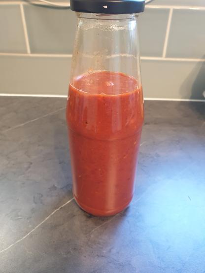 A glass jar of a thick red liquid - a chilli sauce roughly the same texture/thickness as passatta, the red coming from the chillies used