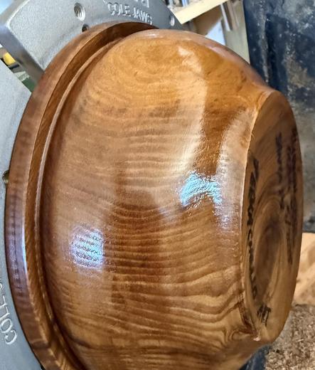 A Russian olive bowl, mounted on Cole jaws on a lathe, with a shiny, but imperfect, shellac and oil finish.