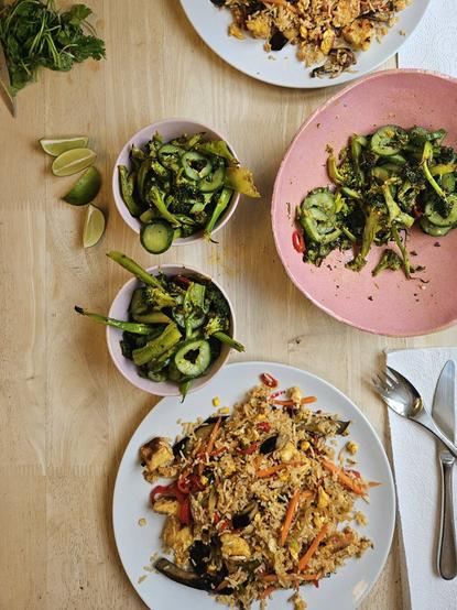 Photo of plates with fried rice and bowls of vegetables on a wooden table