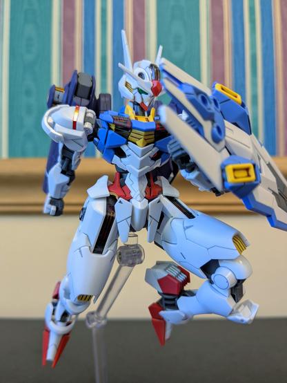 The HG Gundam Aerial (with upside down heels, whoops) advancing toward an opponent to the viewer's left. It is holding its shield in front of it and gripping a prepared beam saber hilt on the Mirasoul