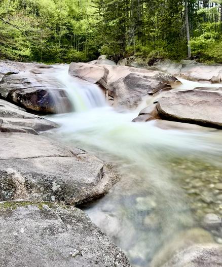 Photo of waterfall in green forested area.  The water is flowing over and between large rock slabs.  Some of the gray slabs of rock are in the foreground.

Franconia Falls.  We saw these falls on a side trip on our return from the campsite.