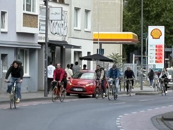 Ein Auto steht auf einem Schutzstreifen, viele Fahrräder fahren drum herum.
