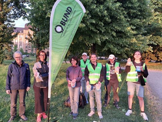 Insgesamt sieben Personen, teilweise mit BUND-Weste ausgestattet, stehen neben einem BUND-Beachflag und präsentieren ihre aufgesammelten Zigarettenkippen. (Foto: Klaus Kurtz)