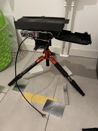 Overview of the setup. Old Zeiss Super Ikonta 532/16 camera for 120 film on the tripod with the lens facing straight to the bathroom floor, distance to the lens about 28cm.
The back cover is open to accept a self made platform of about 30mm height where the negative film is placed. This is neccessary to get the minimal focal distance down as the camera normally has about 1.6m minimum distance.
For ilumination a smartphone was used displaying a white screen on full brightess. I used a mechanical shutter release for exposure.
The image came out 15cm big and the exposure was 8 seconds.