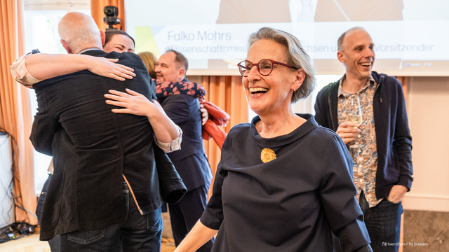 Foto von Rektorin Prof.in Ursula Staudinger bei der Verkündung zu den Exzellenzclustern. Im Hintergrund liegen sich die Clustersprecher:innen in den Armen.
