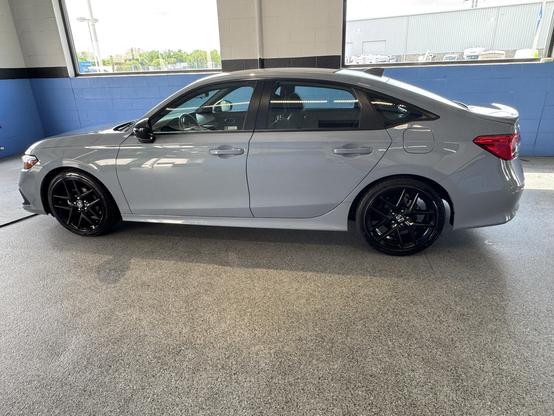 A silver 2023 Honda civic sedan with black wheels parked indoors, showcasing a sleek design against a light gray and blue background.