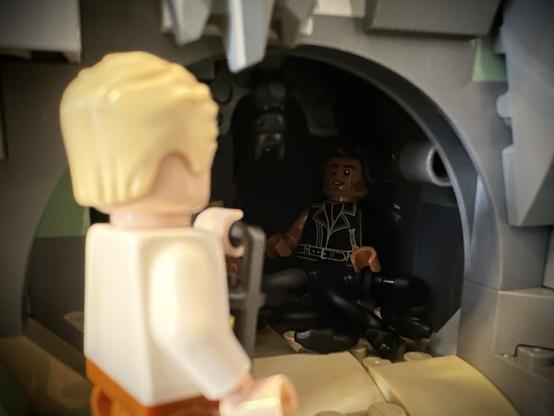 Lego Stede facing away from the camera, holding a lantern while looking into a cave. Inside the cave, Lego MerKraken Ed, with a concerned look on his face.