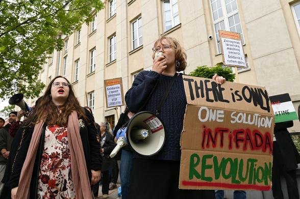 Dwie osoby krzyczące. Jedna z nich, na pierwszym planie, ma ze sobą megafon oraz karton z napisem "There is only one solution, intifada revolution"