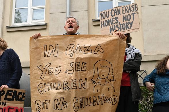 Osoba trzymająca arkusz szarego papieru z napisem "In Gaza you see children but no childhood"