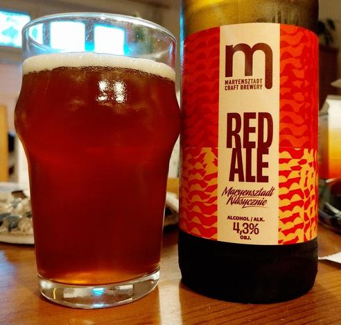 A glass of red ale next to a bottle. Beer made by Browar Maryensztadt.