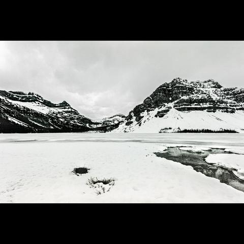 Black and white photo of a mountain and a frozen lake with snow above