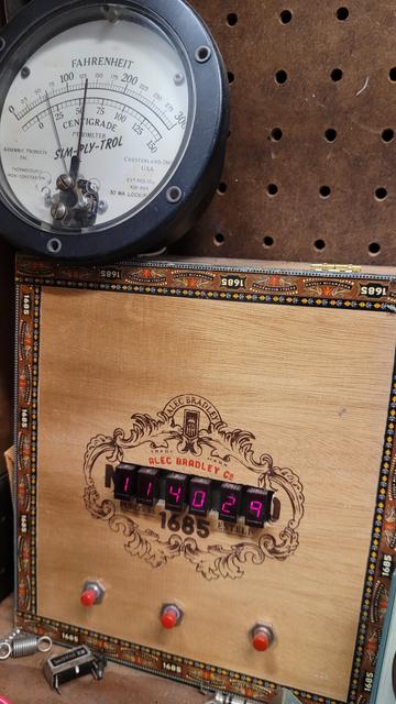 Old school digital readout clock in red next to a temperature gage off some ancient equipment