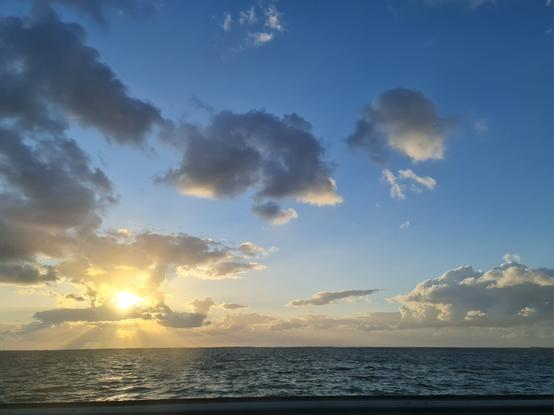 zonsondergang met stalen licht vanachter paar bloemkool wolken in verder blauwe lucht